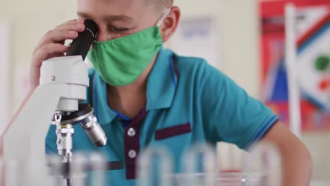 Boy-wearing-face-mask-and-protective-glasses-using-microscope-in-laboratory