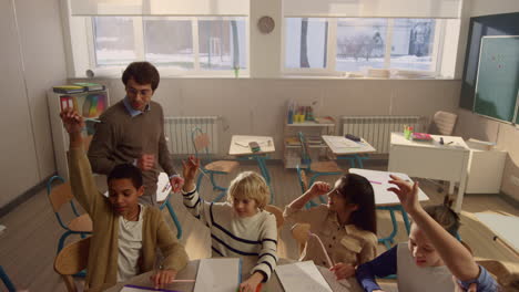 Students-raising-hands-at-lesson-in-classroom.-Schoolteacher-asking-questions