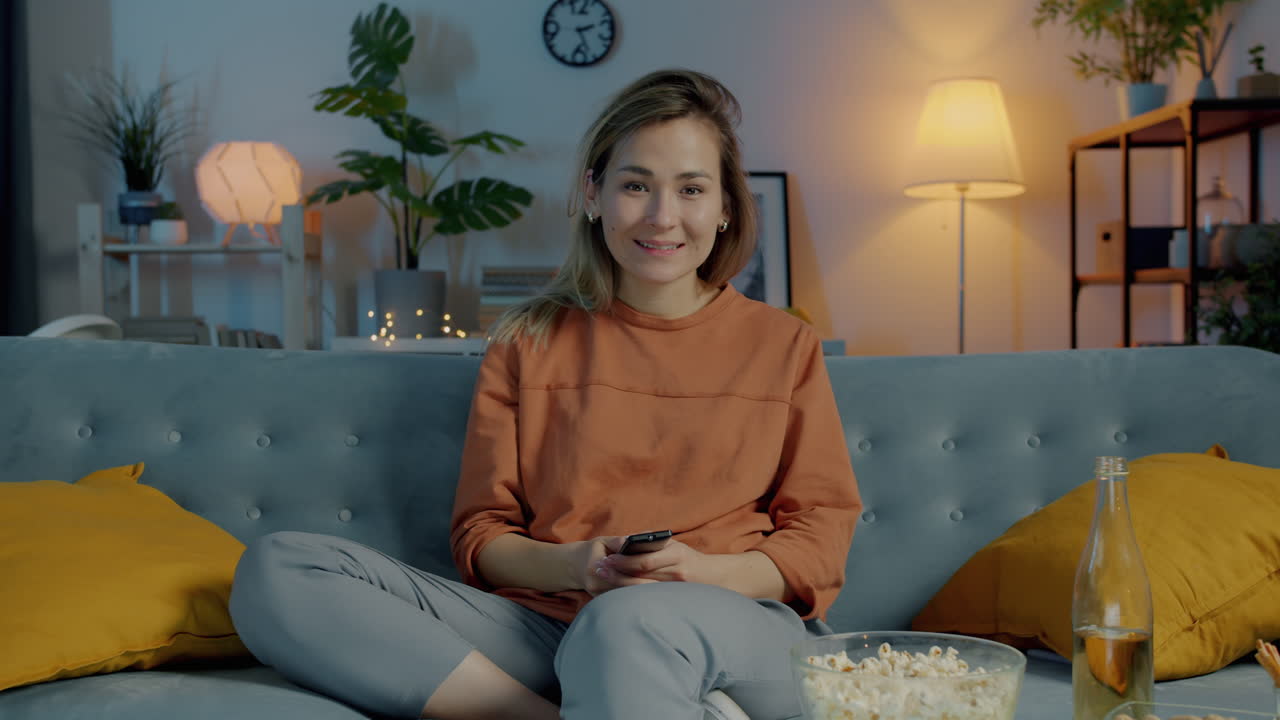 Kvinde slapper af på sofaen, ser tv og nyder popcorn