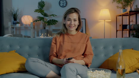 woman relaxing on couch, watching tv and enjoying popcorn