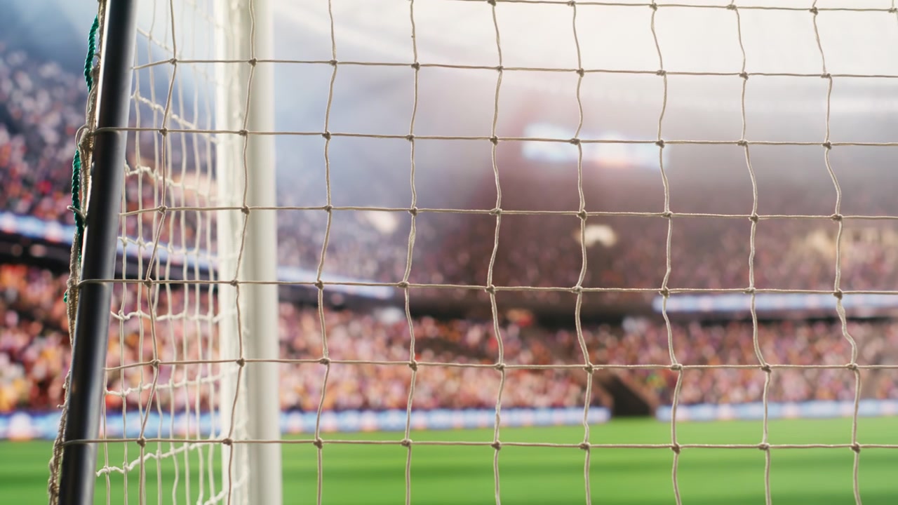 Bulanık tribünlerin olduğu boş sahayı çerçeveleyen açılı futbol kale ağı ve yan direk.