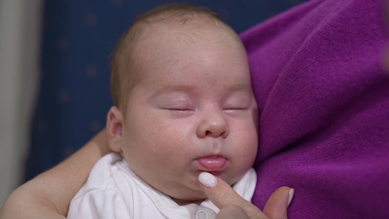 Sweet child sleeping tightly in his mom's hands. Caring momma trying to wake him up by touching little nose lovingly. Adorable sleeping newborn close up.