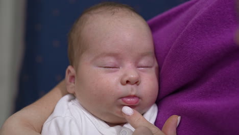 sweet child sleeping tightly in his mom's hands. caring momma trying to wake him up by touching little nose lovingly. adorable sleeping newborn close up.