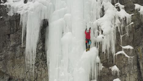 Mountain-climber-on-frozen-cascade-progressing-towards-peak