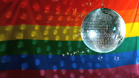 Bola-De-Discoteca-Brillante-Girando-Con-Burbujas-Flotantes-Contra-La-Bandera-Del-Arco-Iris