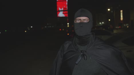 caucasian man in full black cape and hood mask costume at night in bahrain