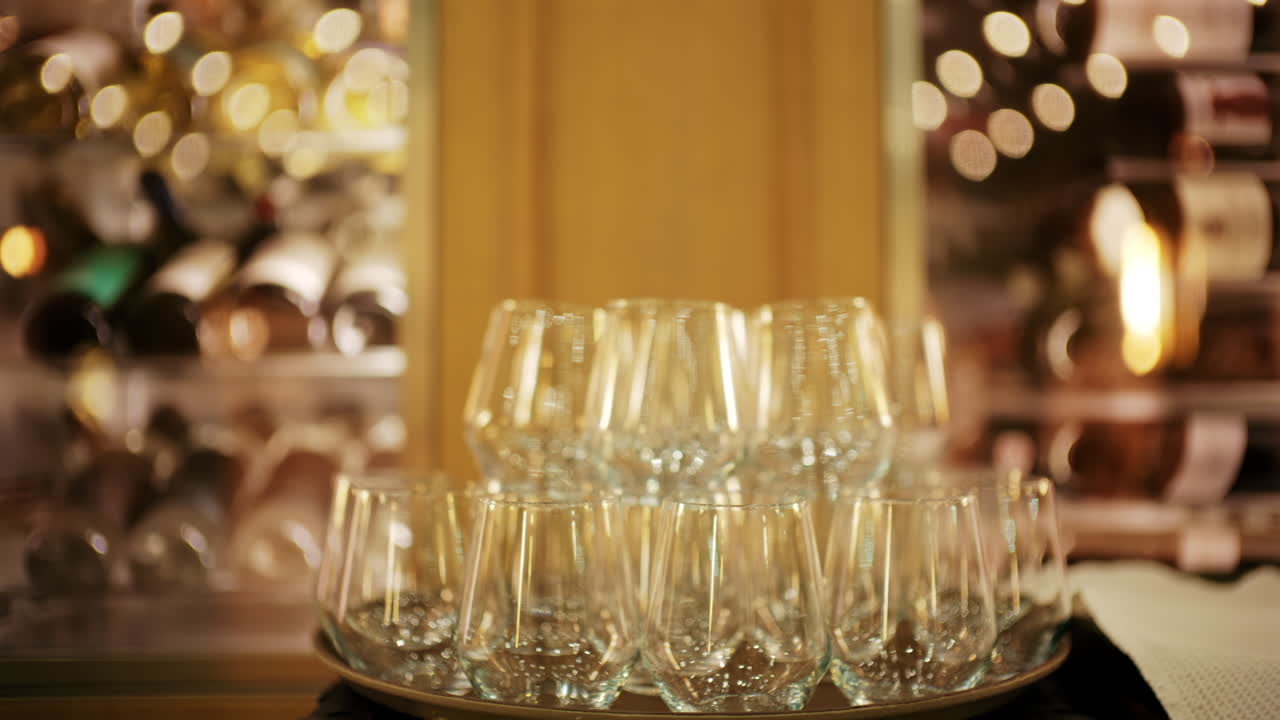 Elegante vinglas arrangeret på en bakke i et blødt oplyst restaurantmiljø, med vinreoler sløret i baggrunden.
