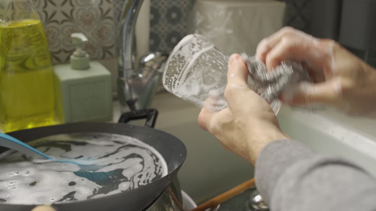 Lavare un bicchiere sporco con una spugna sopra un lavello della cucina
