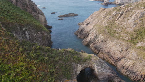 Luftaufnahme-Der-Wunderschönen-Wilden-Klippenküste-An-Einem-Sonnigen-Tag,-Während-Meereswellen-Auf-Den-Felsen-Brechen