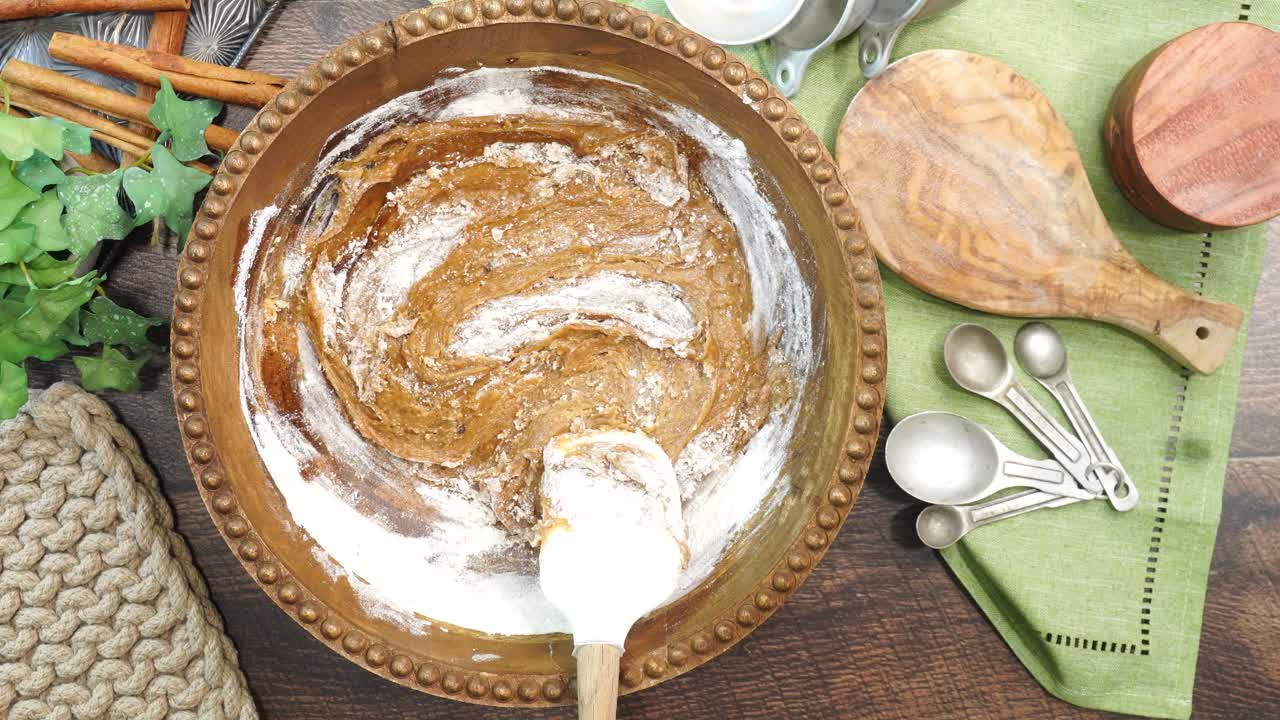 Baking a carrot cake loaf with cream cheese icing and topped with roasted salted pecans. Making a Autumn dessert with carrots, flour, sugar, nuts and frosting. Mixing in the flour to the batter.