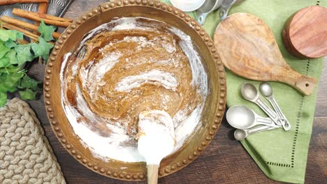 baking a carrot cake loaf with cream cheese icing and topped with roasted salted pecans. making a autumn dessert with carrots, flour, sugar, nuts and frosting. mixing in the flour to the batter.