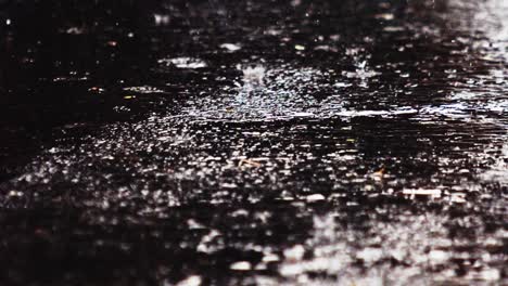 light rain water droplets falling on dark asphalt road, close up ground shot