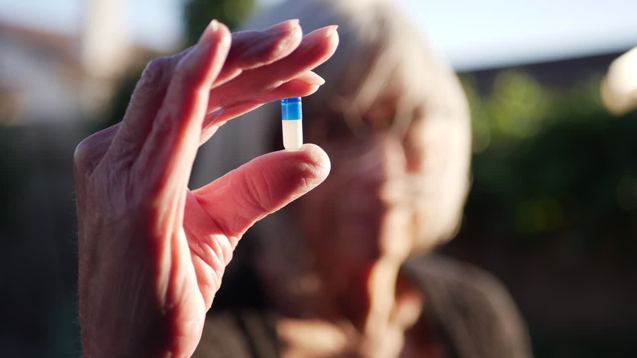 Una donna anziana che tiene una pillola blu di un farmaco su prescrizione per curare il suo cancro.