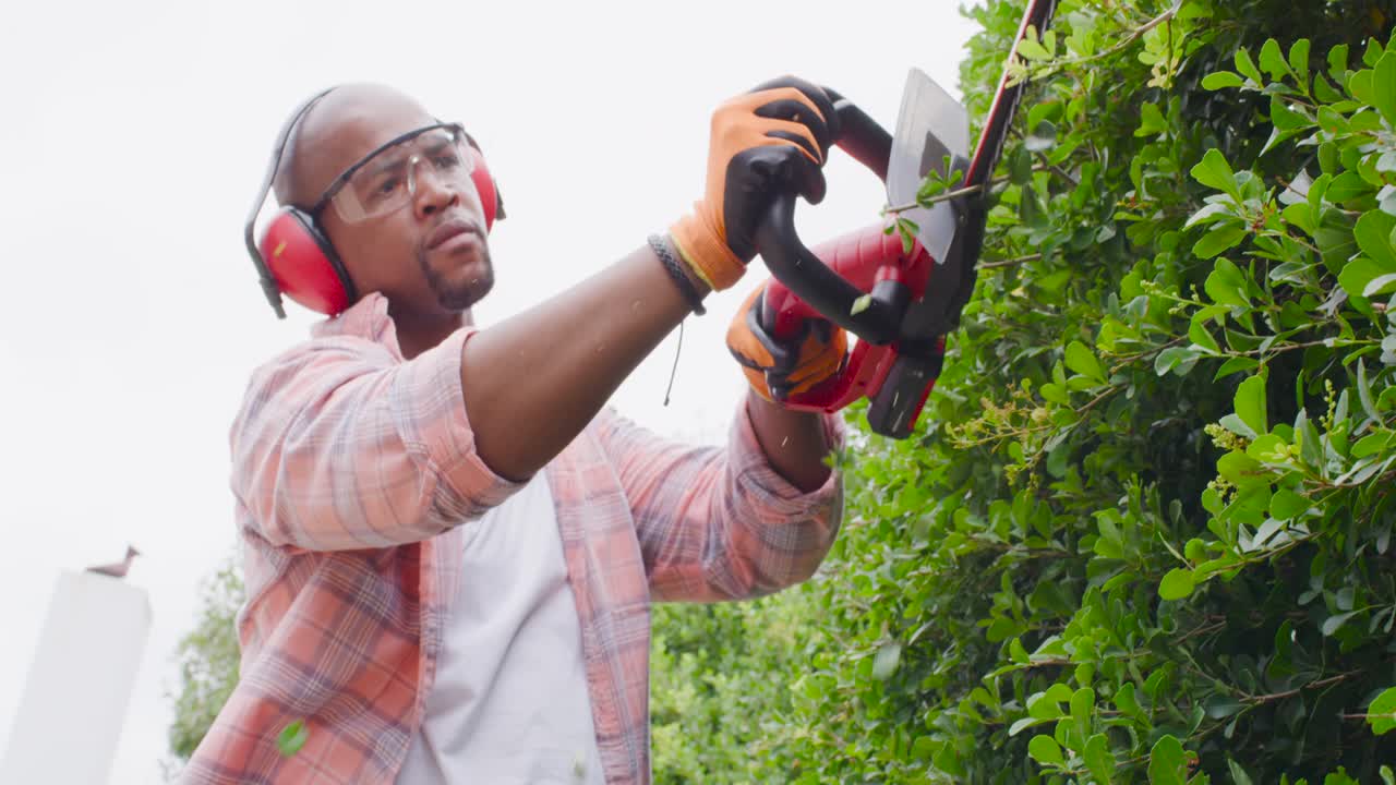 Man raising red hedge trimmer trimming hedge shaping yard beside path with gloves, copy space