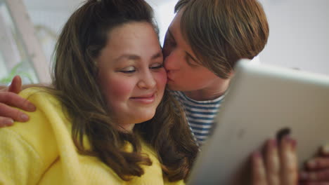 Young-Downs-Syndrome-Couple-Sitting-On-Sofa-Watching-Digital-Tablet-At-Home