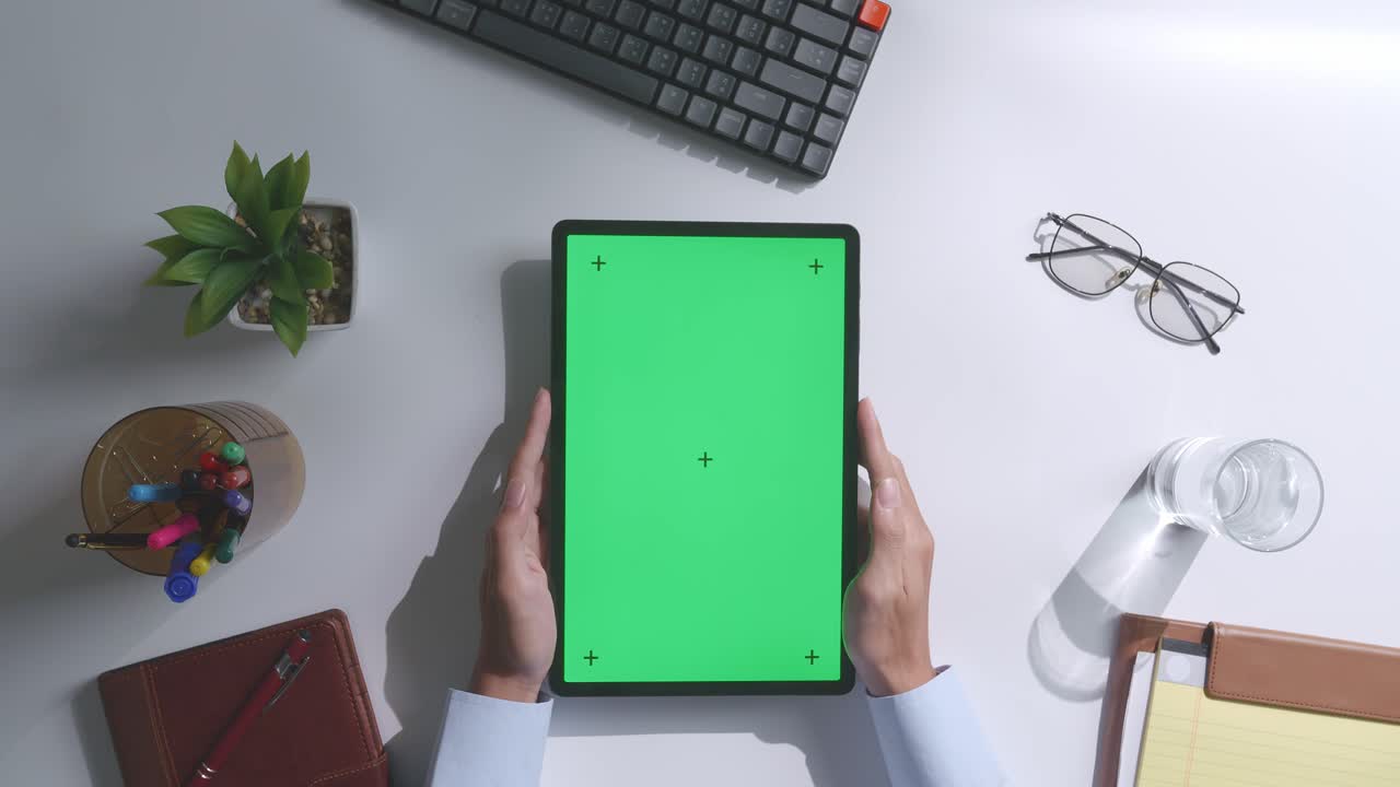 vista de arriba hacia abajo de una computadora portátil con pantalla verde simulada pantalla chromakey en un escritorio de oficina de madera al lado de la libreta con bolígrafos, gafas y un vaso de agua.