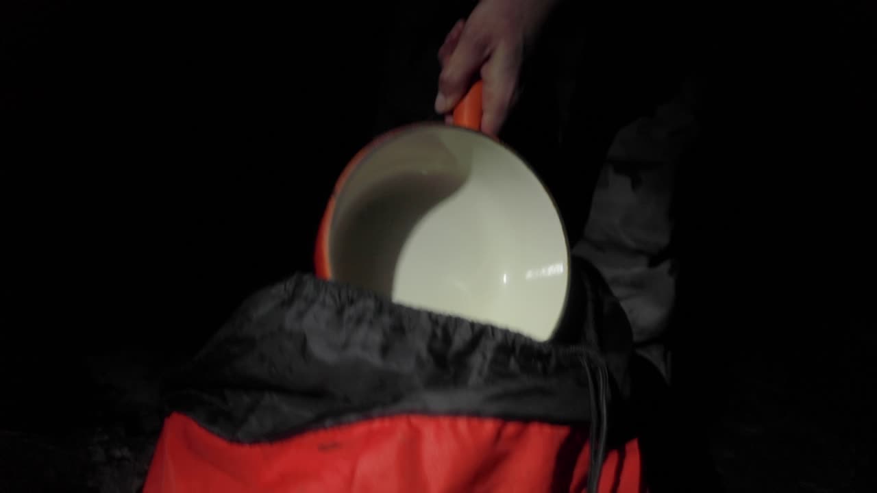 cámara lenta, persona sacando la sartén de la mochila mientras acampa por la noche