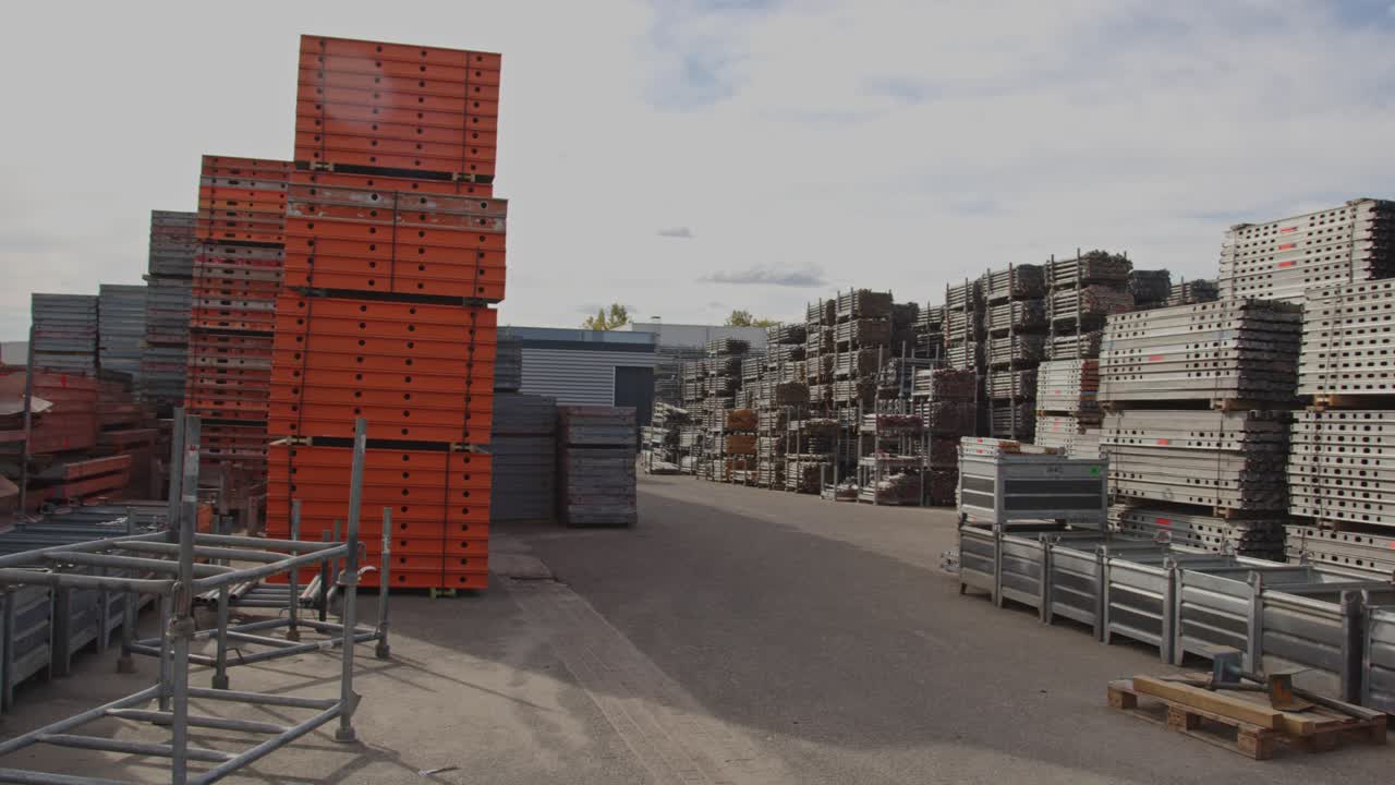 Pan of a large industrial storage yard filled with stacks of material and scaffolds on a sunny day