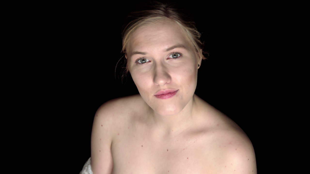 joven mujer rubia está de pie sobre fondo negro y mirando a la cámara