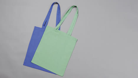 Primer-Plano-De-Bolsas-Azules-Y-Verdes-Sobre-Fondo-Gris,-Con-Espacio-Para-Copiar,-Cámara-Lenta