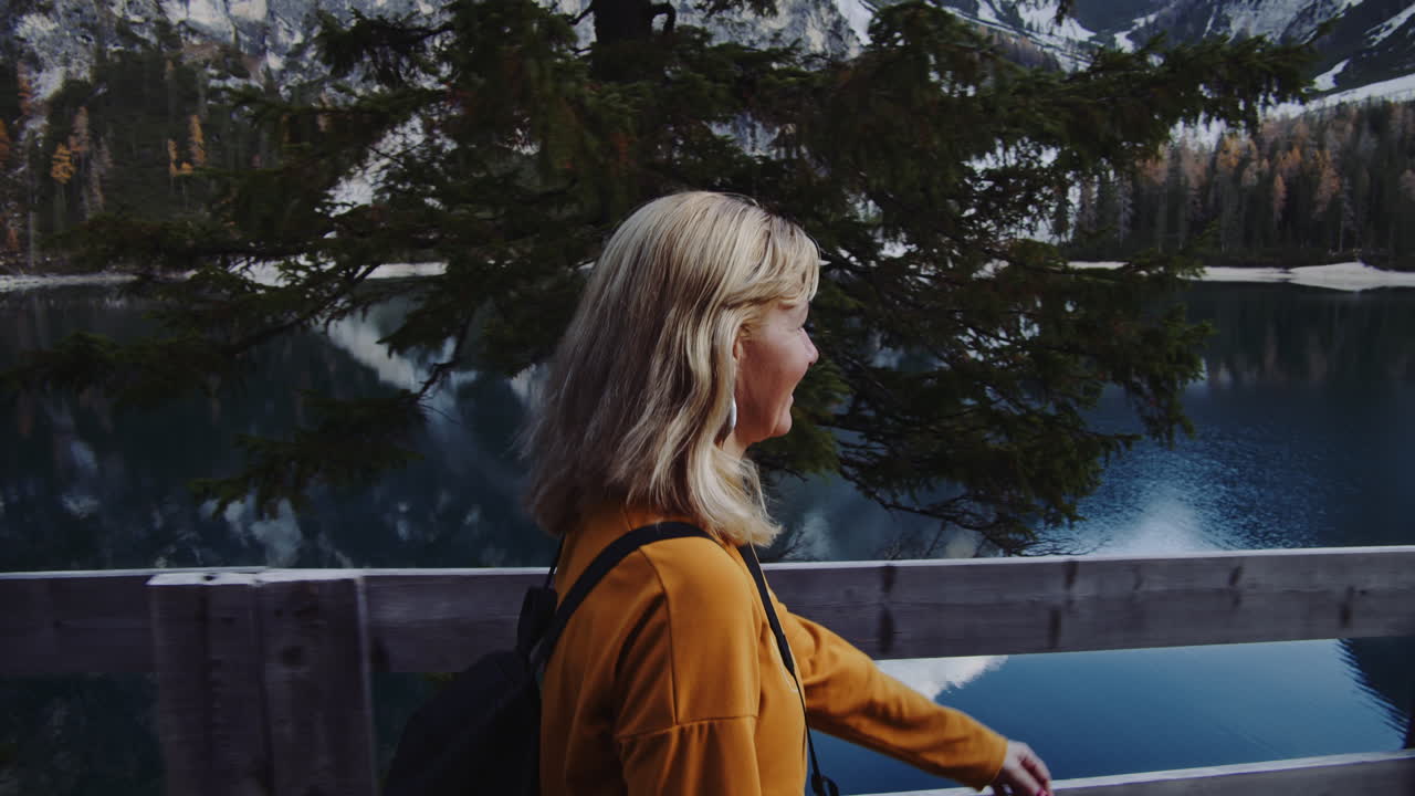 A blond haired woman walks along the shore of the lake laughing