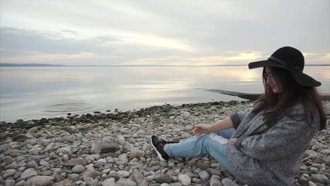 mujer sentada en una playa de guijarros al atardecer