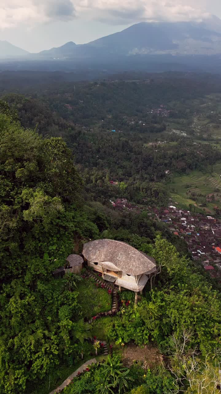 Vertical drone footage showing a unique bamboo home on the hillside of Sidemen, Bali. The villa blends sustainable architecture with incredible volcano and forest views