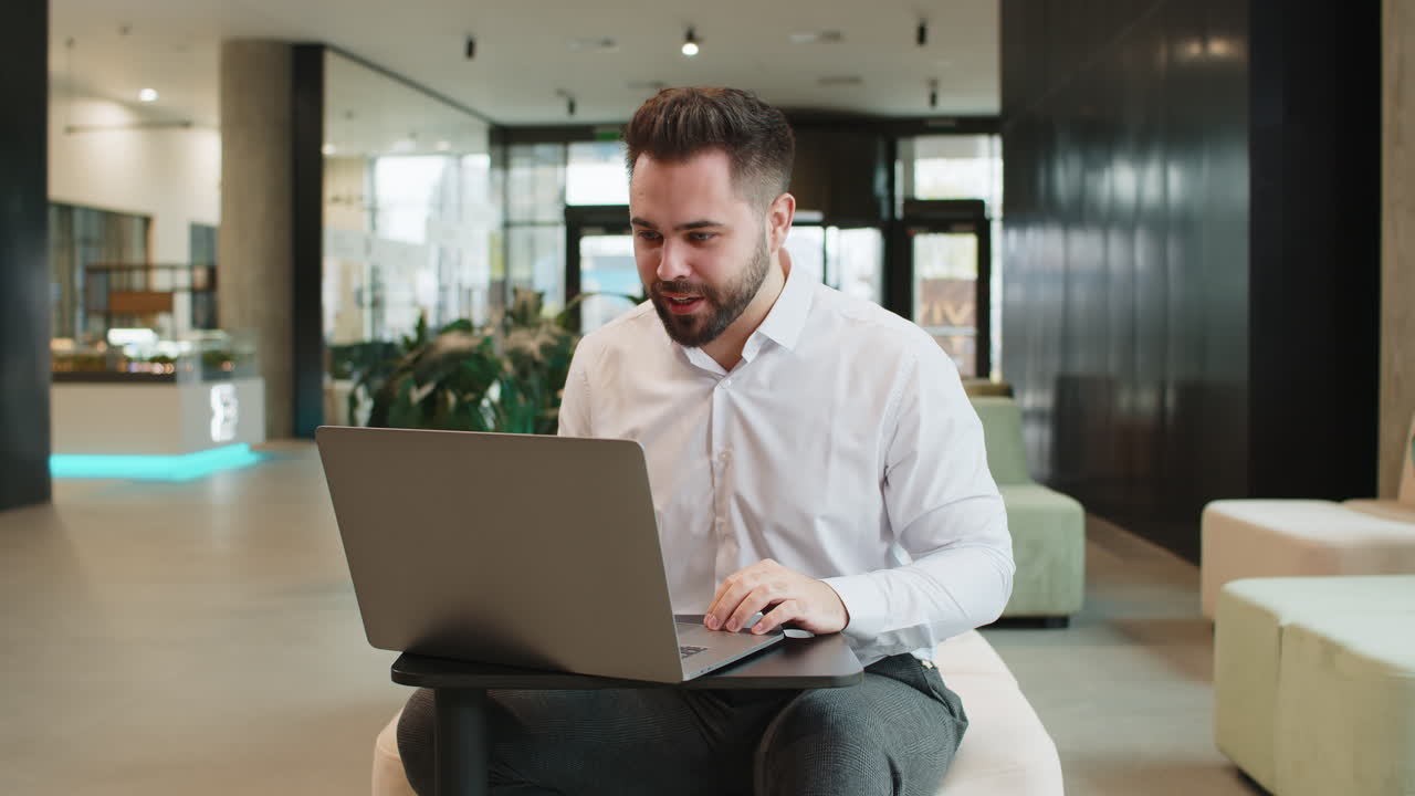 Young businessman using laptop talking on online communication video call in modern office lobby