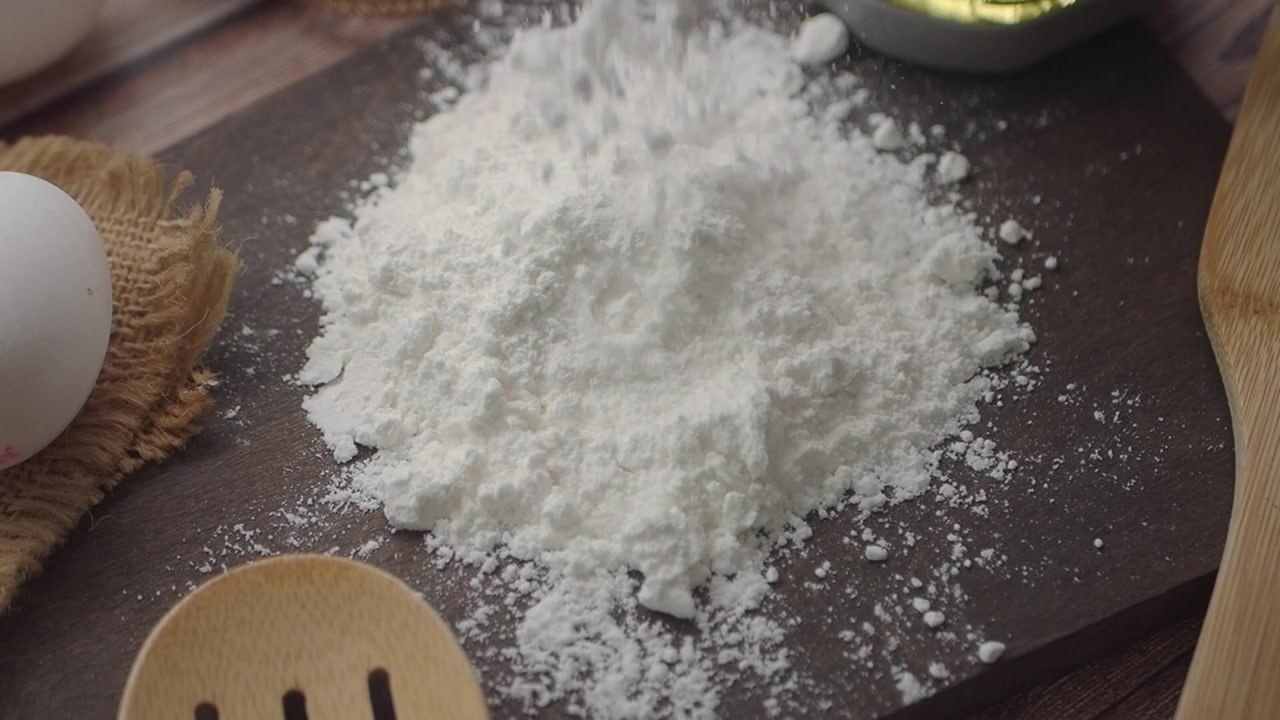 Farina bianca che si sparge su un tagliere di legno con ingredienti da forno