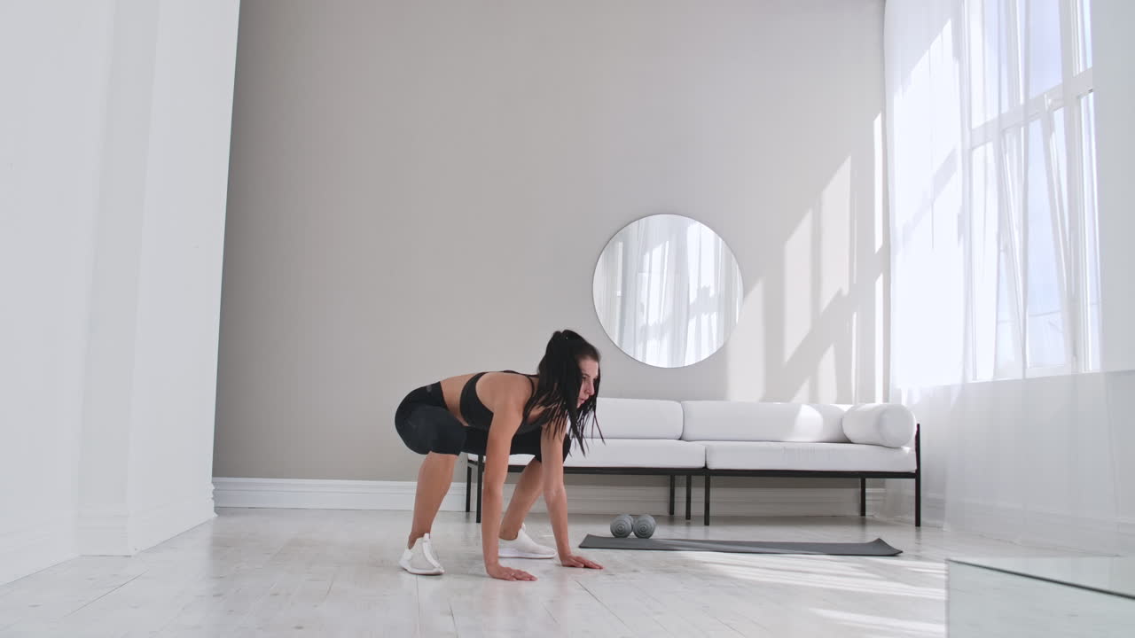 hermosa mujer delgada de treinta años con complexión clara hace ejercicios de esfuerzo matutino y burpee aeróbico en una habitación moderna y aireada