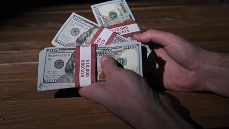 male hands hold three stacks of 10000 us dollar bills on wooden background