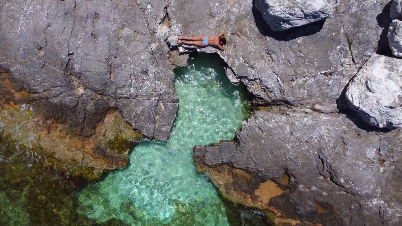 piscina de mar abierto en forma de corazón en una playa rocosa, niña tomando el sol