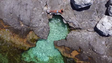 heart-shaped open sea pool on a rocky beach, girl sunbathing