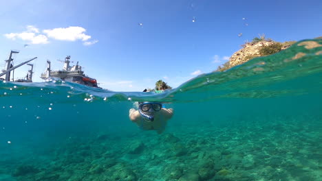 Mittlere-Zeitlupenaufnahme-Einer-Jungen-Frau-Mit-Schnorchel-Und-Schutzbrille,-Die-An-Einem-Sonnigen-Tag-Im-Meer-Schwimmt-Und-In-Richtung-Kamera-Taucht