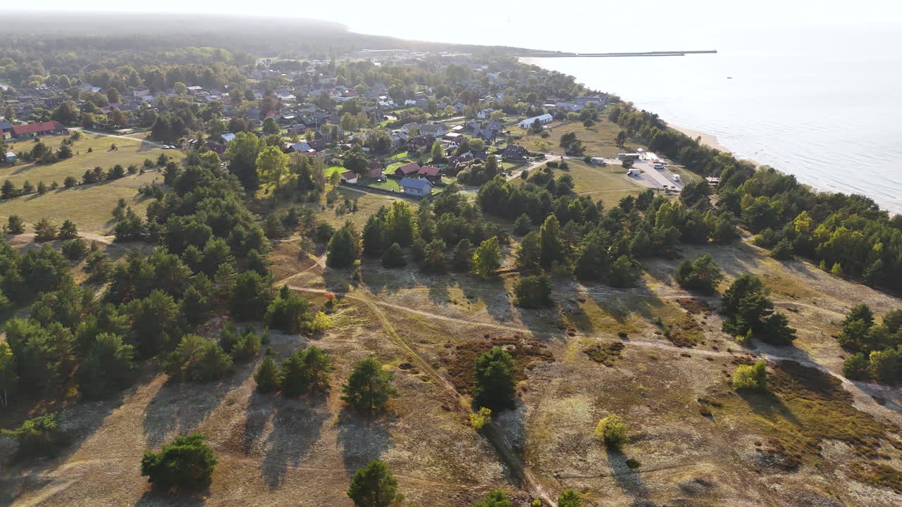 High aerial ascend over undulating dunes and pine forest near Pavilosta coast in warm golden daylight