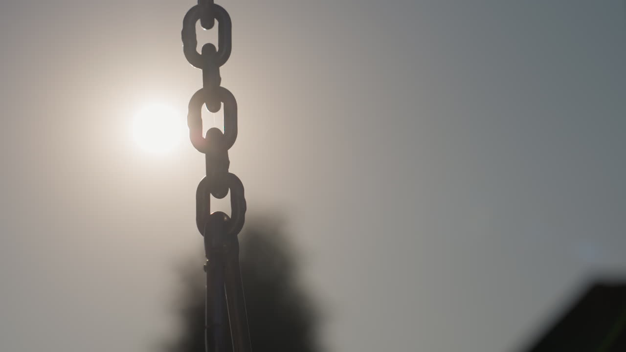Bright Sky Highlights Swing Chain, Backlit Chain Against Glowing Sun Creates Playful Silhouette Mood, Silhouette Of Swing Chain Illuminated By Bright Sun Against Moody Sky Evoking Nostalgia