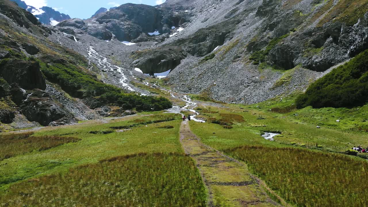 A shot of people walking in a valley landscape with a glacier and snow peaks