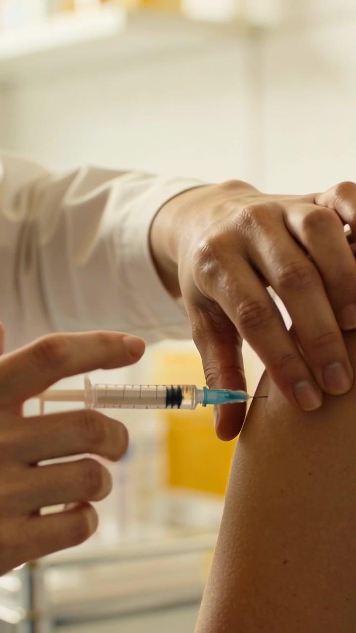 Vertical video: Syringe nearing arm in clinic, clinician in white coat injecting and giving dose