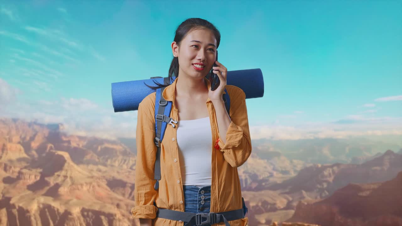 Asian Female Hiker With Mountaineering Backpack Smiling And Talking On Smartphone While Traveling At The Top Of Mountain