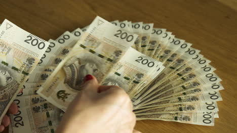 Female-hands-counting-a-stack-of-the-200-Polish-zloty-bills-at-the-table---business-and-finance-concept-close-up-shot