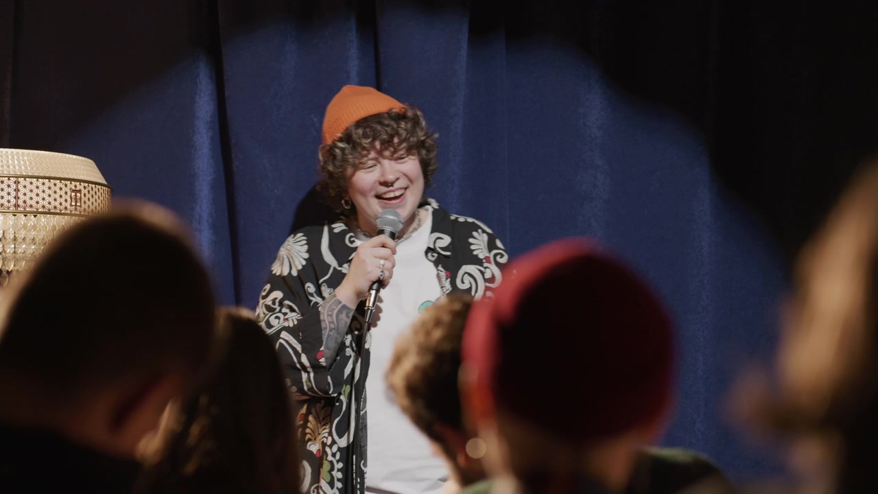 Ung kvindelig standupkomiker fortæller en historie og griner på scenen.