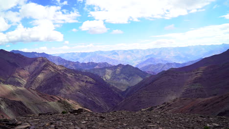 Push-in-shot-towards-the-edge-of-a-mountain,-beautiful-panoramic-view-with-endless-mountain-range-under-a-bright-sky-with-few-clouds