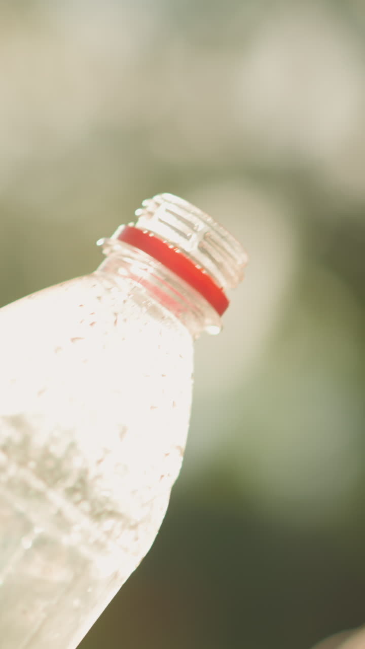 primer plano de una mujer bebiendo jugo de naranja al aire libre de una botella de plástico con satisfacción relajada, la luz del sol reflejándose en la botella y su mano, un suave resplandor de luz y vegetación en el fondo