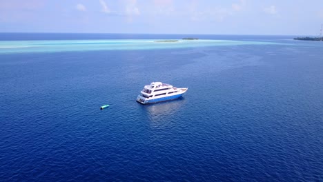 ferry approaching slowly toward seashore of tropical island in the middle of deep blue ocean surrounded by shallow turquoise waters of maldives