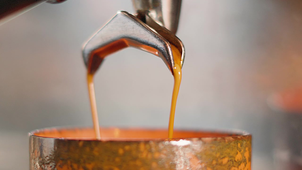 Friskkværnet kaffe hældes i kop fra portafilter for at lave en Flat White. Højkvalitets slow motion-klip af professionel barista, der laver varm morgendrik.