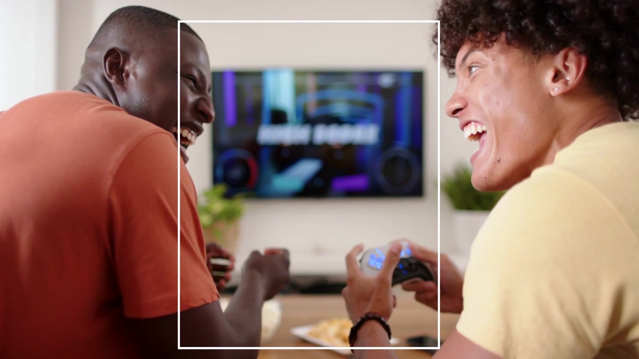Two men gaming at table, right man using controller causing binary overlay, fading, laughing
