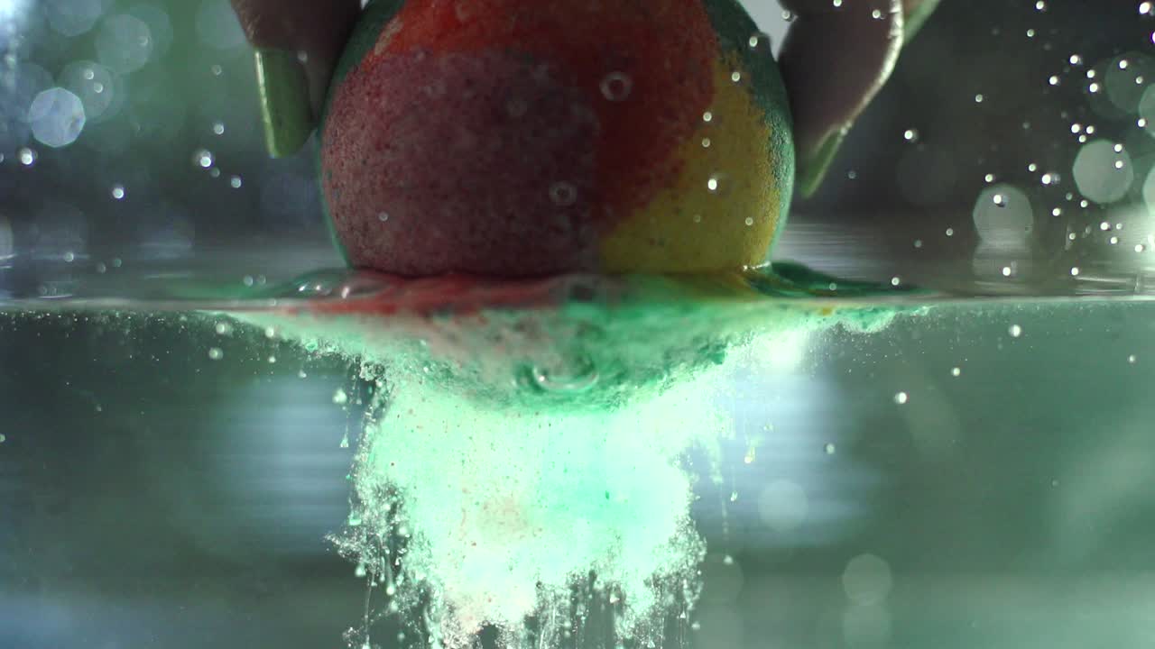 un clip en cámara lenta de una bomba de baño colorida colocada en una tina transparente para que puedas ver cómo se activa lentamente y burbujea en el agua