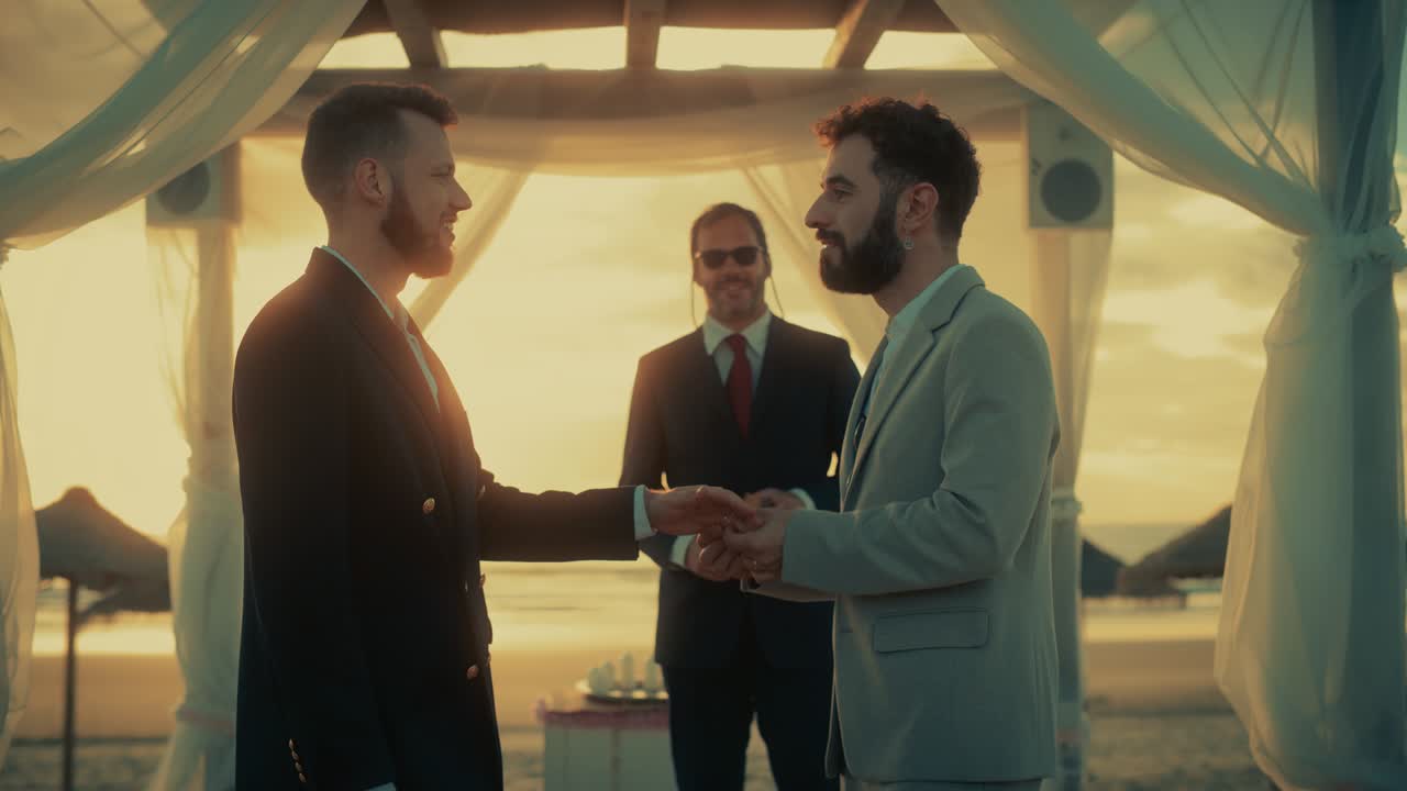 Close Up of Handsome Gay Couple Exchange Rings and Kiss at Outdoors Wedding Ceremony Venue Near the Sea. Two Happy Men in Love Share Their Vows and Get Married. LGBTQ Relationship Goals.