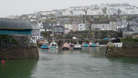 The-entrance-to-Mevagissey-Harbour-waterfront-with-moored-boats-on-a-typical-overcast-day-in-Cornwall,-England,-UK