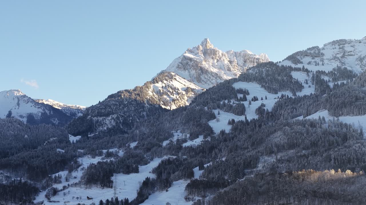 Sluncem zalitý alpský vrchol nad zasněženými zalesněnými svahy poblíž Walensee pod jasnou zimní oblohou